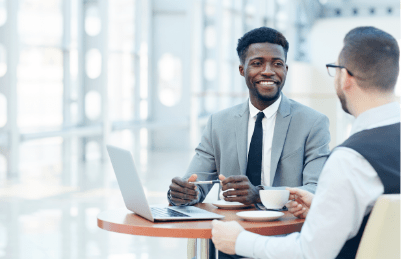 A man drinks his coffee as he talks to his advisor as he presents something on his laptop.